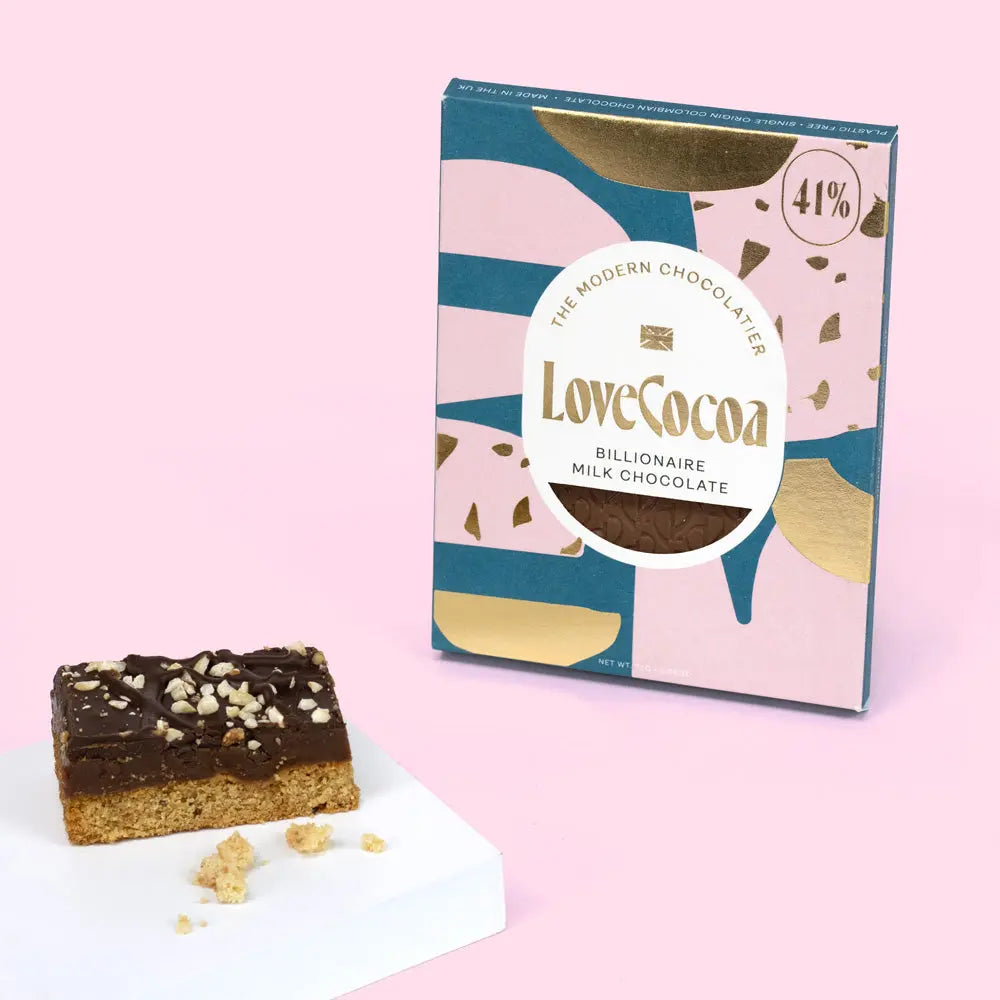 Love Cocoa Billionaire Milk Chocolate Bar 70g, pack with a slice of millionaire shortbread on a pink background