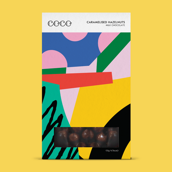 COCO Caramelised Hazelnuts in milk chocolate, front of box with window on a yellow background