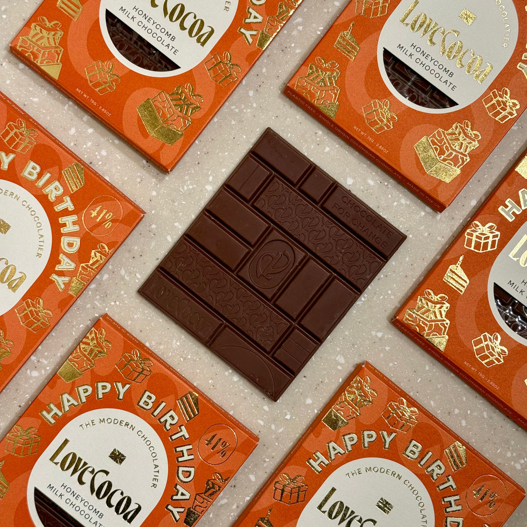 Love Cocoa Happy Birthday Honeycomb Milk Chocolate Bar, unwrapped bar on a stack of Happy Birthday packs