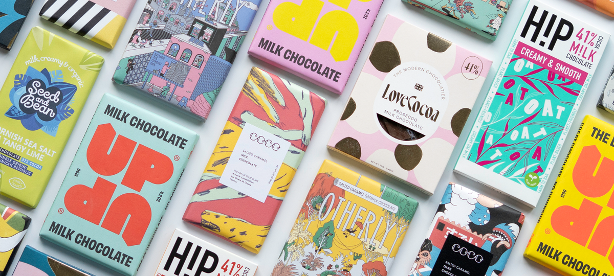 A close-up, angled flat-lay of multiple colorful milk chocolate bars with vibrant, artistic packaging. Visible brands include Up, Hip, Coco, and LoveCocoa.
