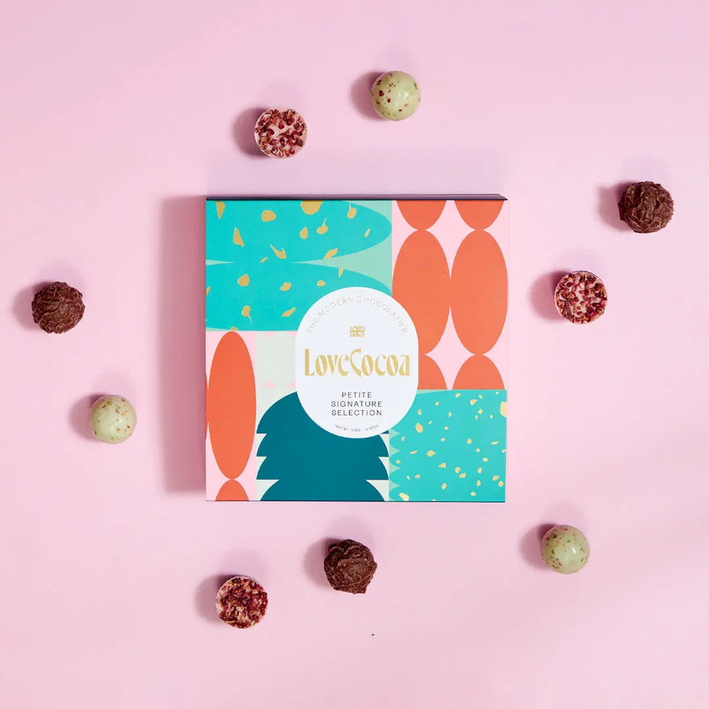 Love Cocoa Petite Signature Selection Box, gift box surrounded by truffles on a pink background