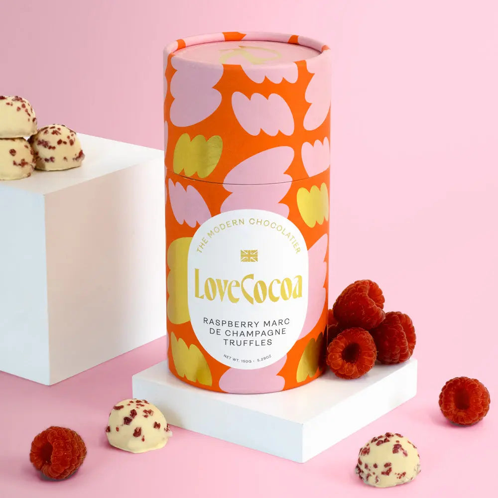 Love Cocoa Raspberry Marc de Champagne White Chocolate Truffles, truffle tube with raspberries and truffles on a pink background