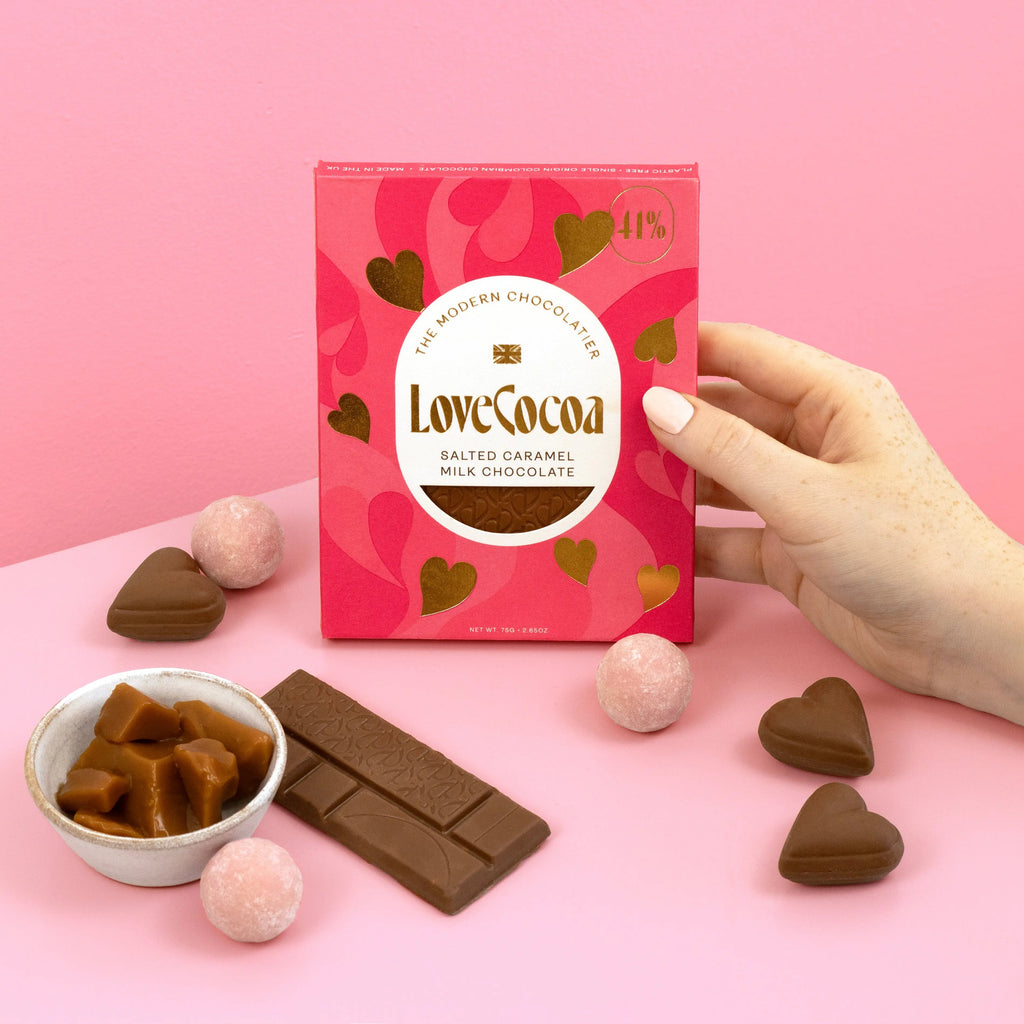Love Cocoa Hearts Salted Caramel Milk Chocolate Bar, pack held in hand with caramel and truffles on a pink background