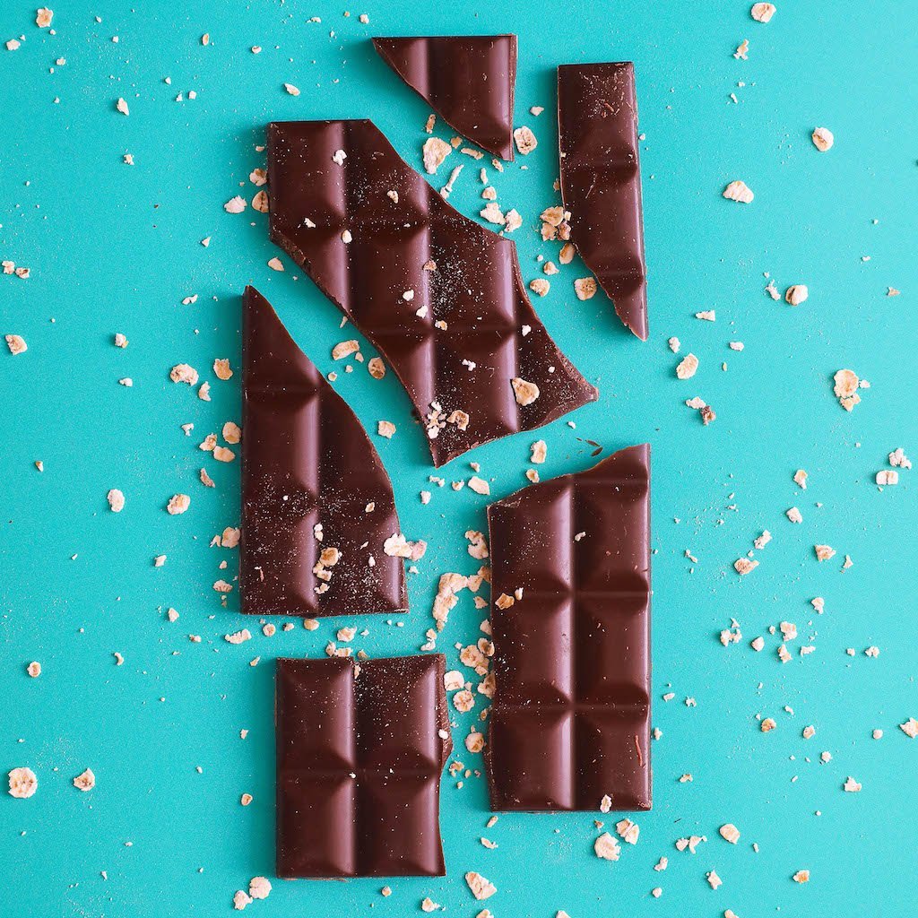 H!P Creamy Original Oat M!lk Chocolate bar, broken chocolate pieces with oat flakes on a turquoise background