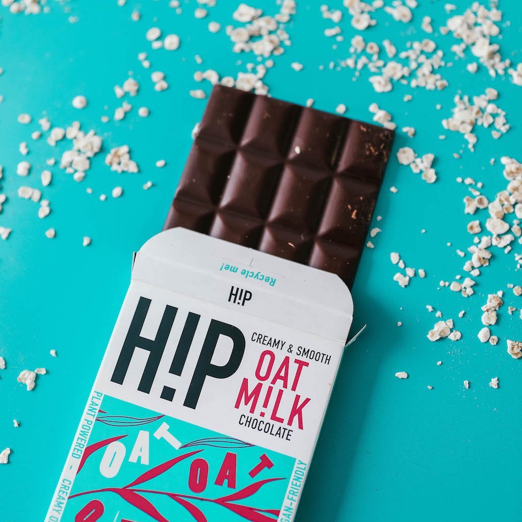 H!P Creamy Original Oat M!lk Chocolate bar, bar half out of its wrapper with oat flakes on a turquoise background